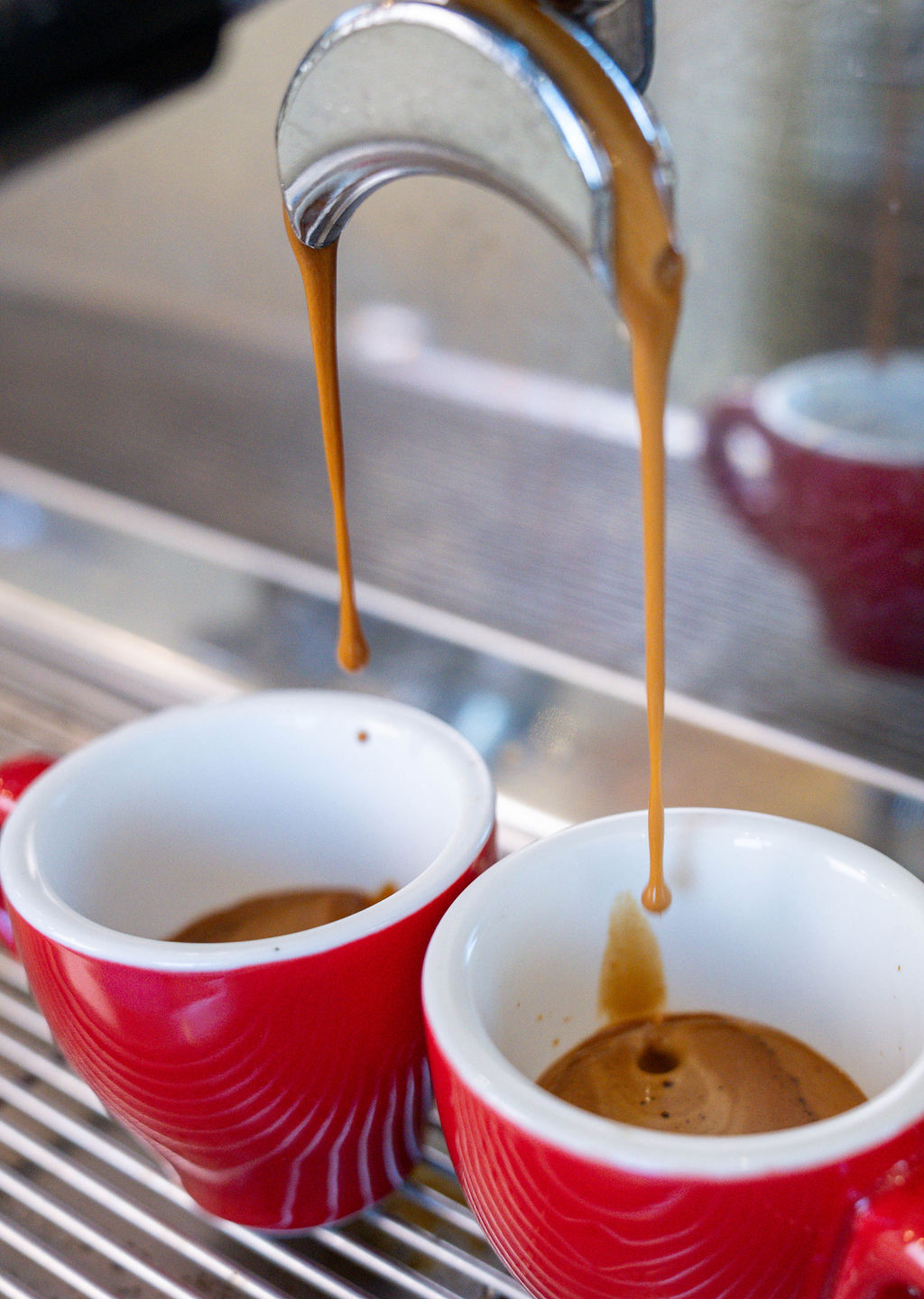Espresso pouring into two red cups
